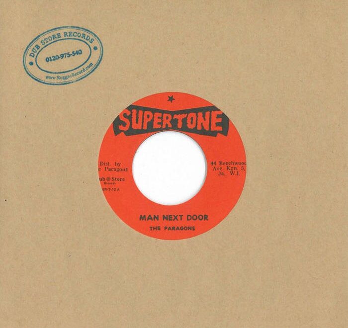 Disco de vinilo de la canción "Man Next Door" de The Paragons, lanzado por Supertone Records. El disco presenta un diseño distintivo con un fondo marrón y una etiqueta roja.