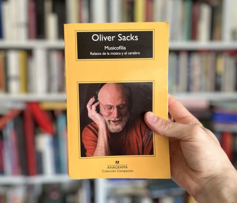 Libro "Musicofilia" de Oliver Sacks, que explora la relación entre la música y el cerebro, sostenido en una mano frente a una estantería llena de libros.
